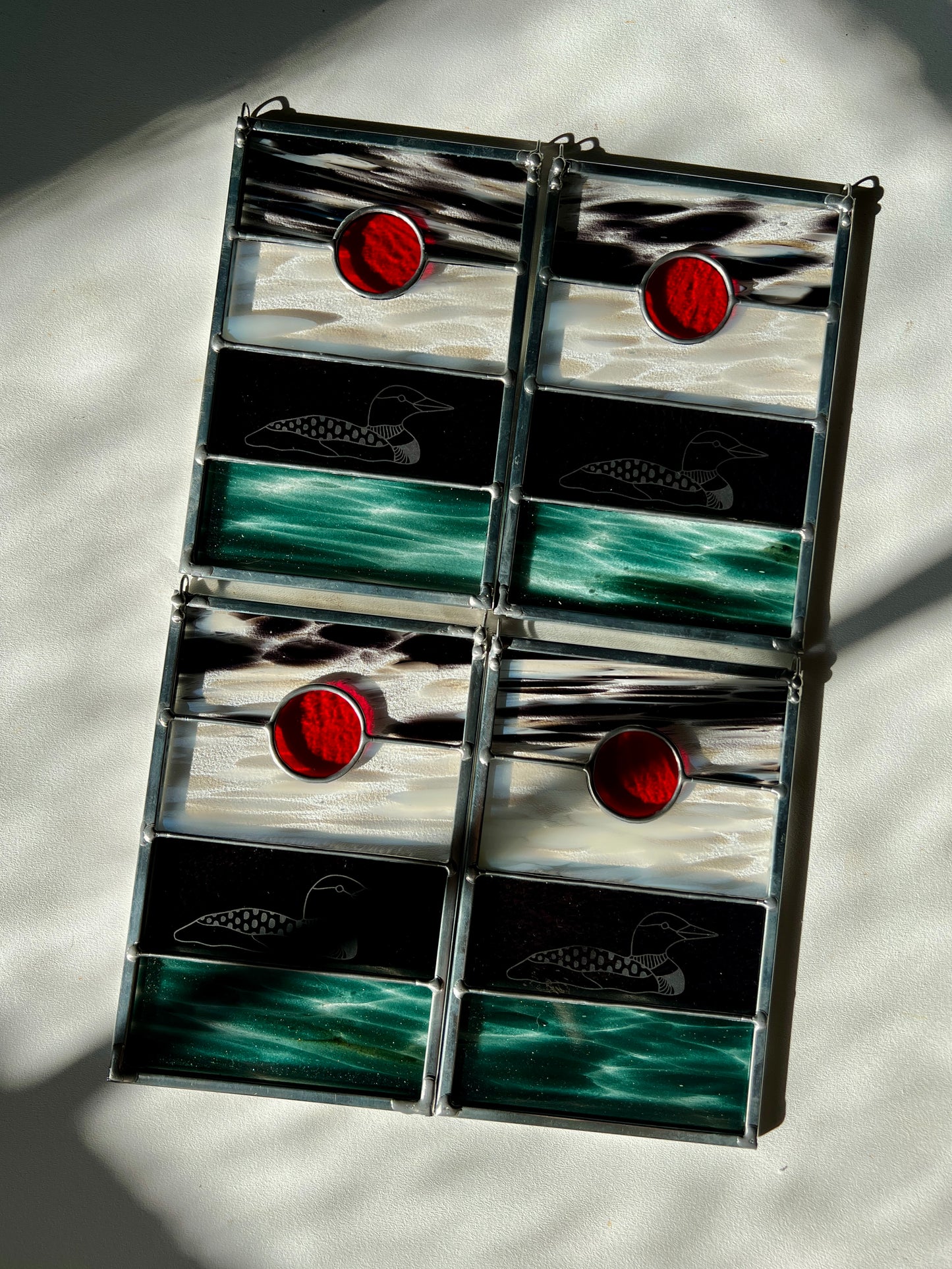 four stained glass panels with black, white, clear, teal, and red glass with loons etched on the surface