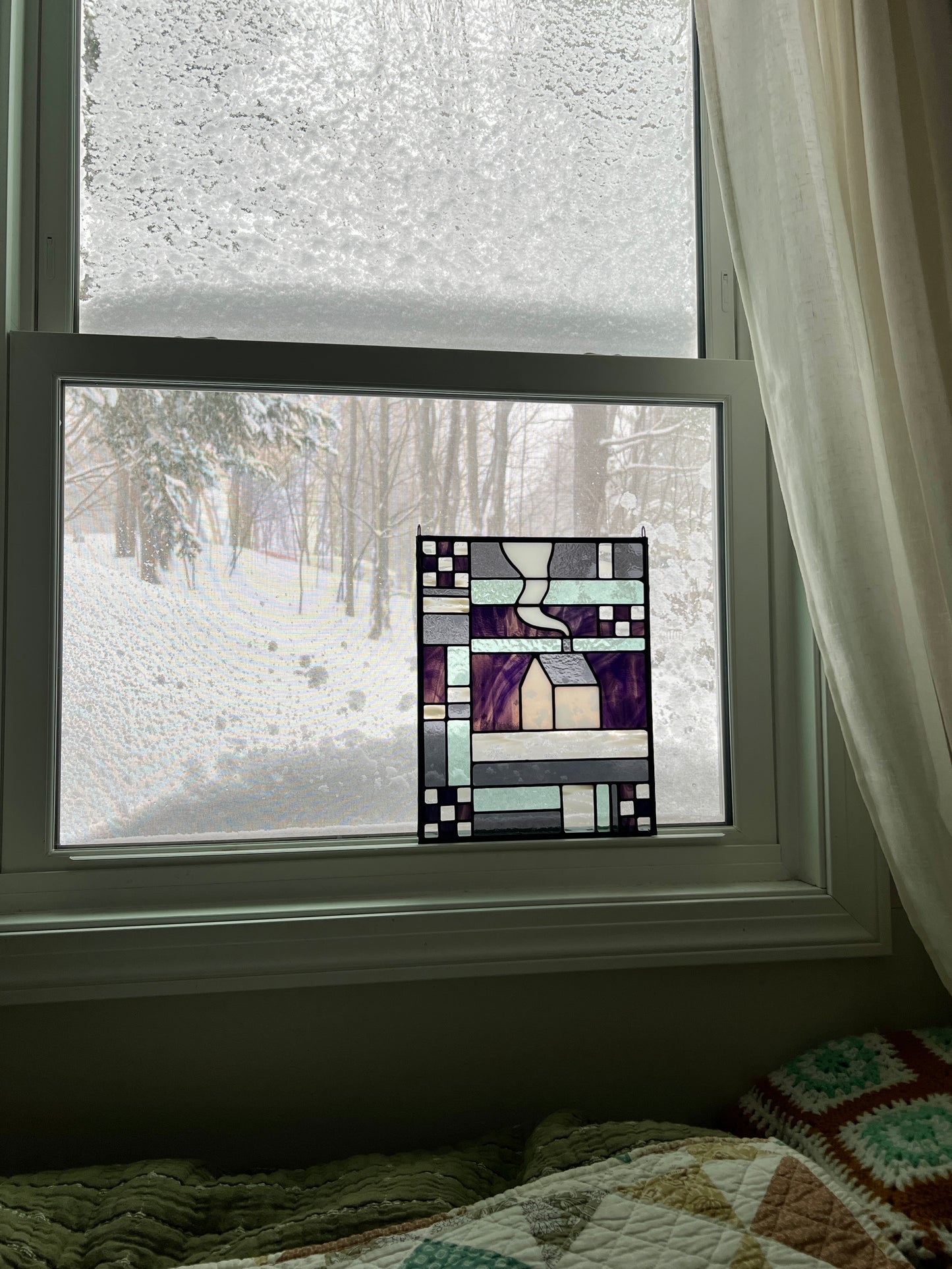 Stained glass textile inspired geometric panel leaning in a window with a snow landscape outside.