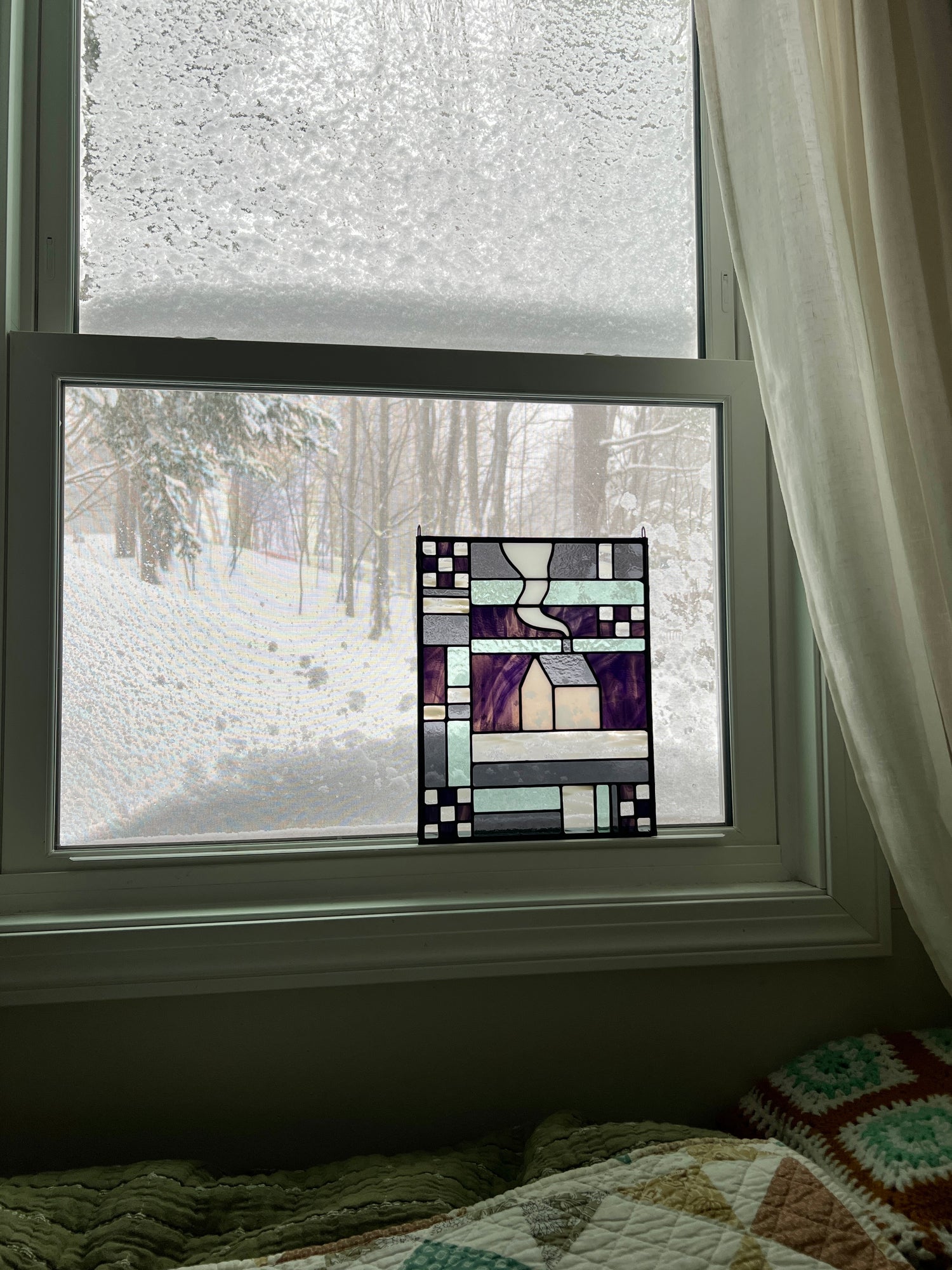 Stained glass textile inspired geometric panel leaning in a window with a snow landscape outside.
