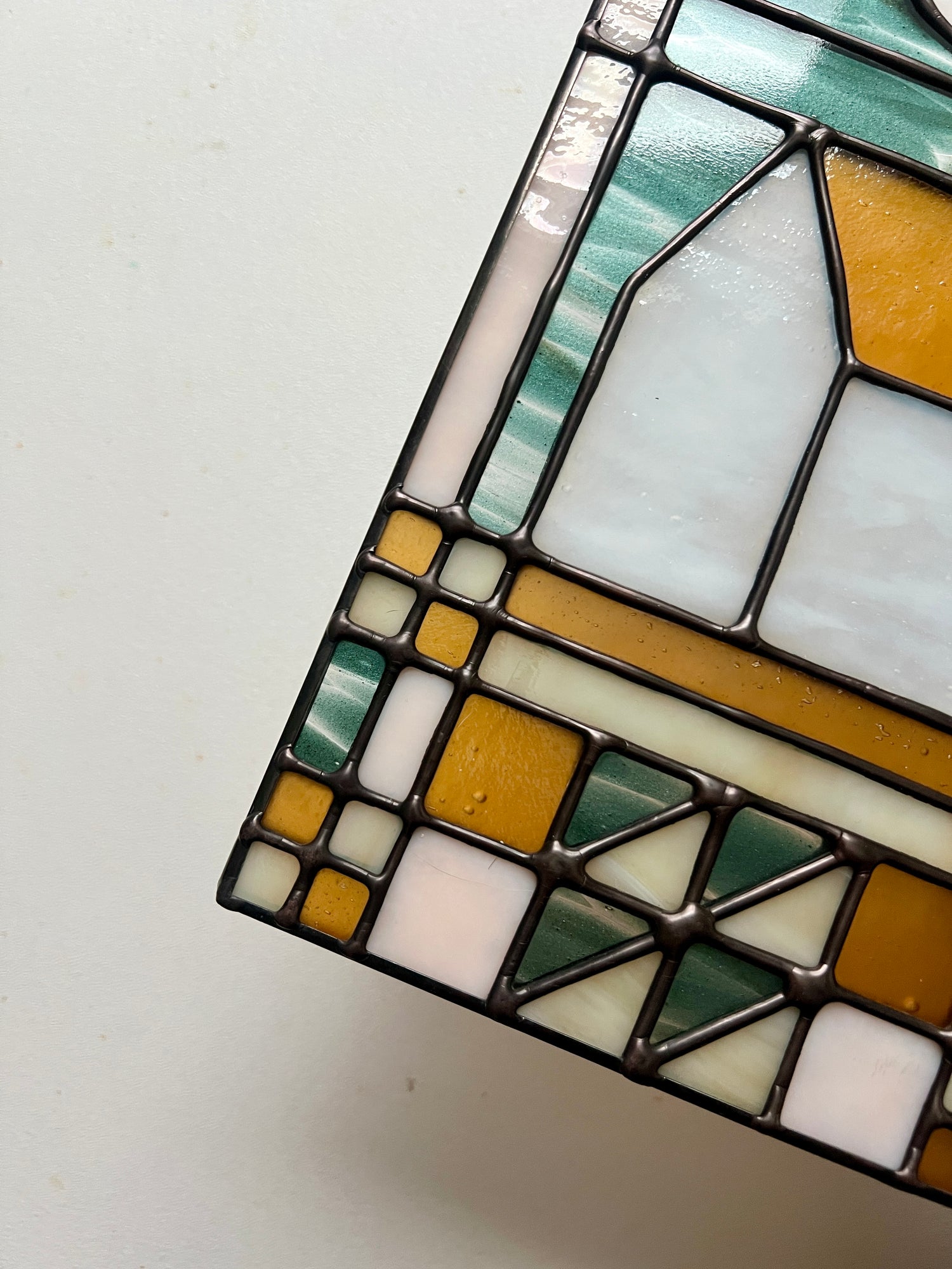 Close up of smooth solder lines on a textile inspired stained glass panel, held above a white surface