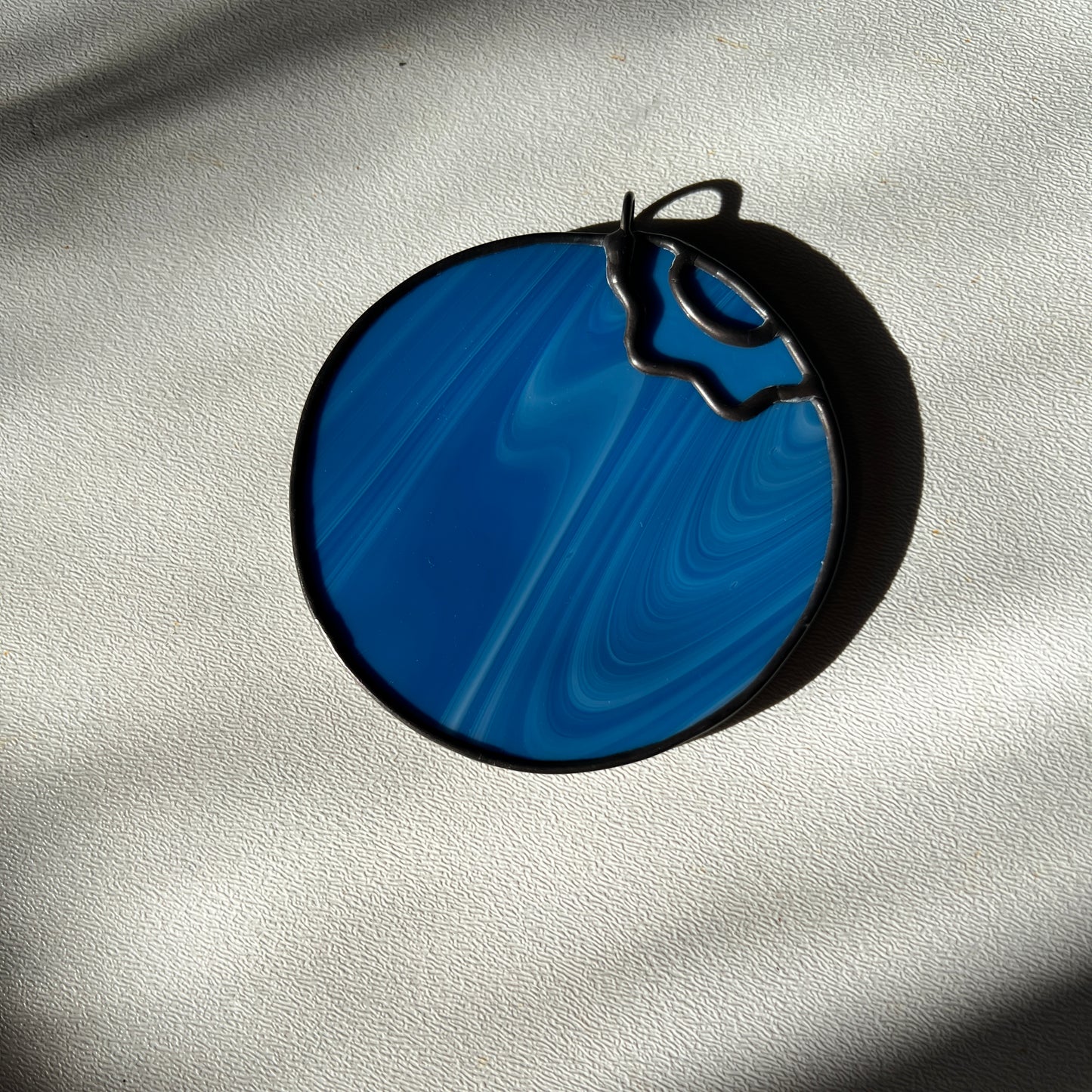  a small streaky blue blueberry suncatcher resting on a white surface