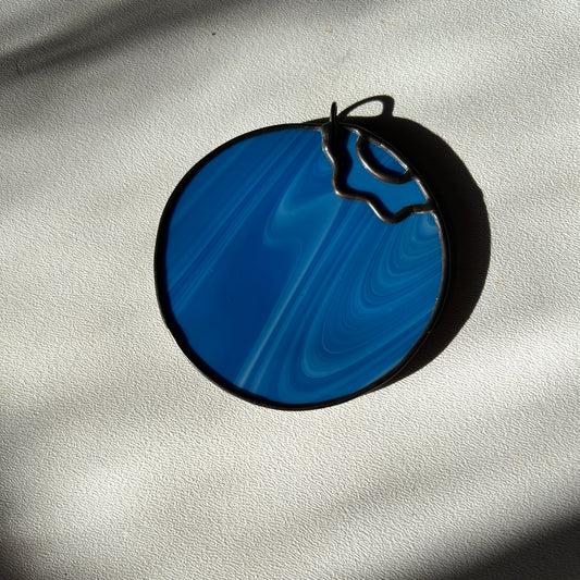  a small streaky blue blueberry suncatcher resting on a white surface