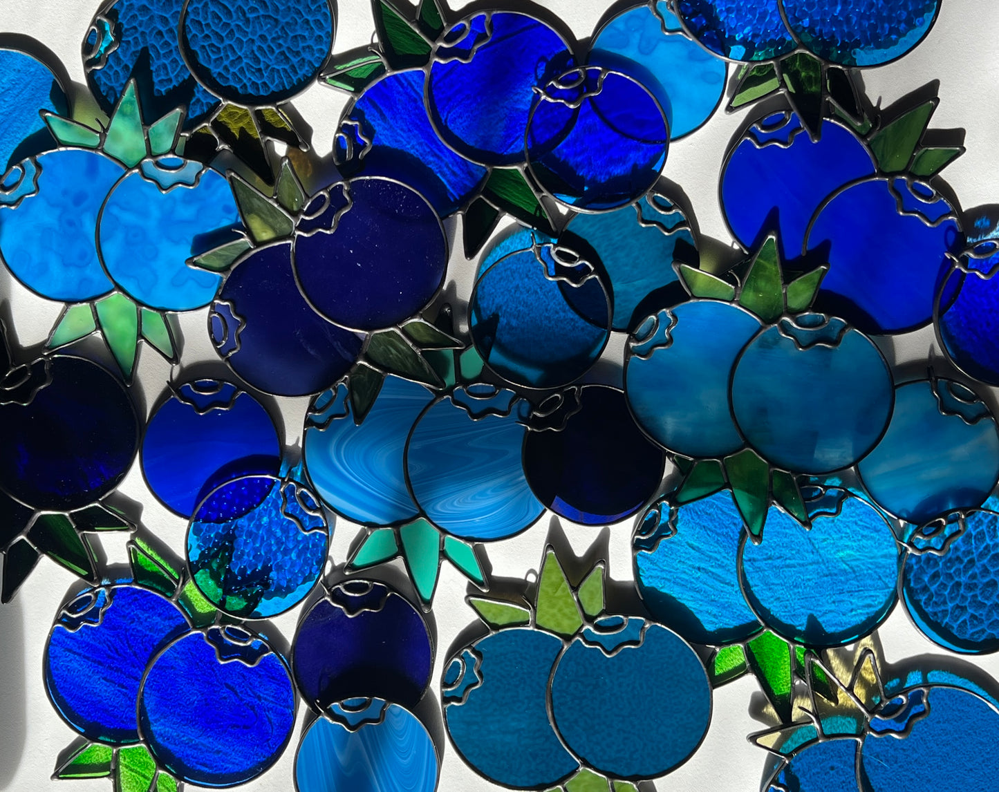 several stained glass blueberries spread out across a white surface
