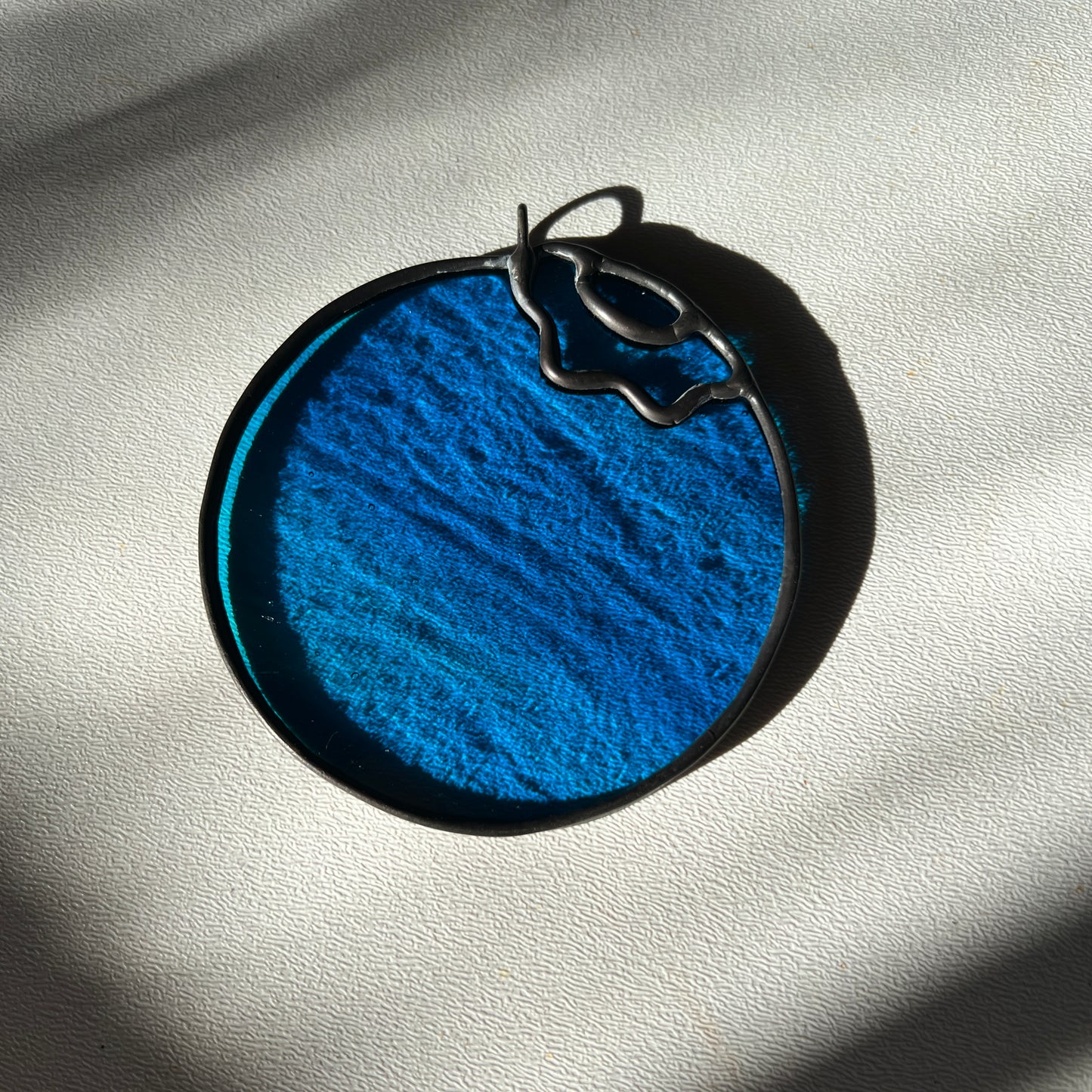 a wispy blue stained glass blueberry resting on a white surface