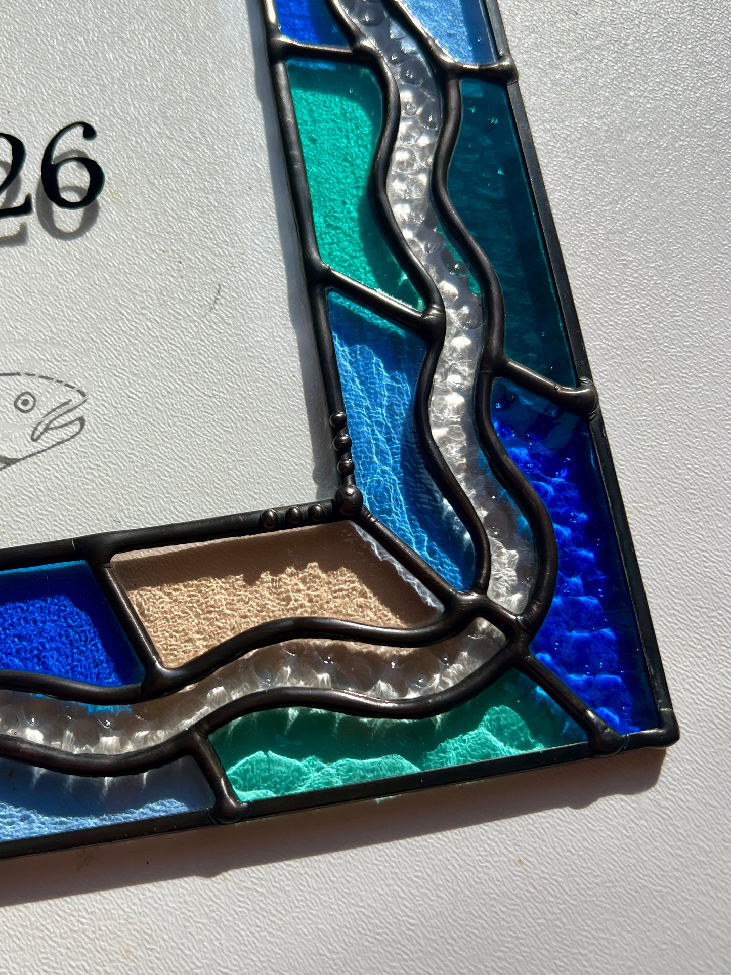 Close up of the solder details of a stained glass piece, with bright blue, green, and pinking glass in the border.