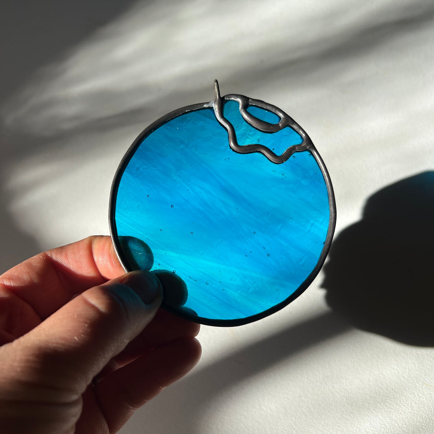 hand holding a wispy blue stained glass blueberry