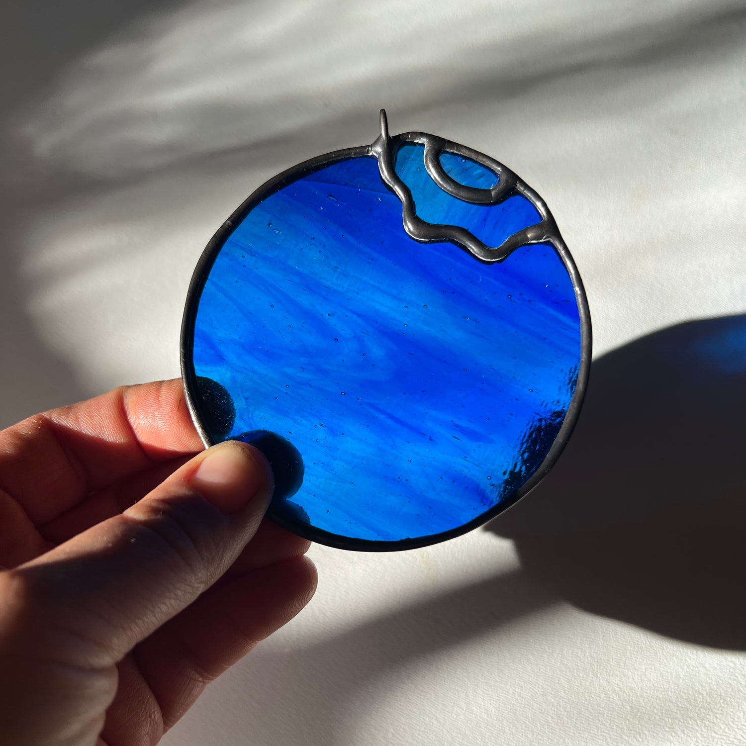 hand holding a wispy blue stained glass blueberry