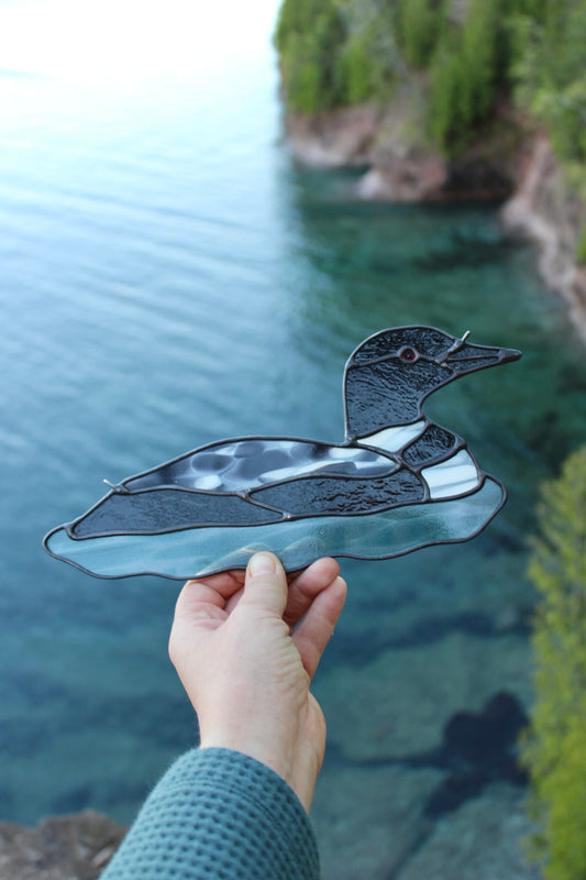 hand holding a stained glass loon high above a rocky Lake Superior shoreline