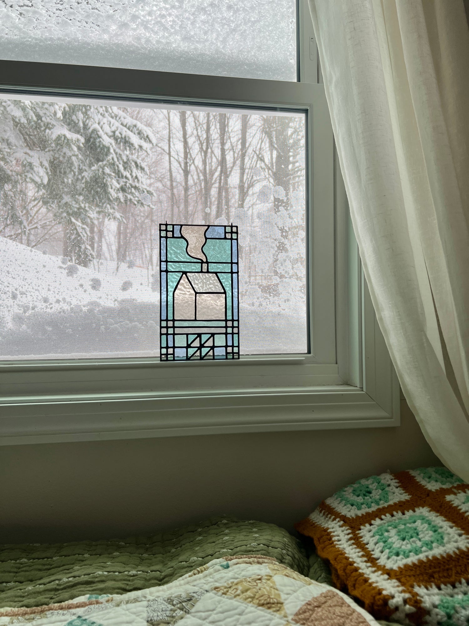 textile inspired stained glass sitting in the window of a cozy bedroom