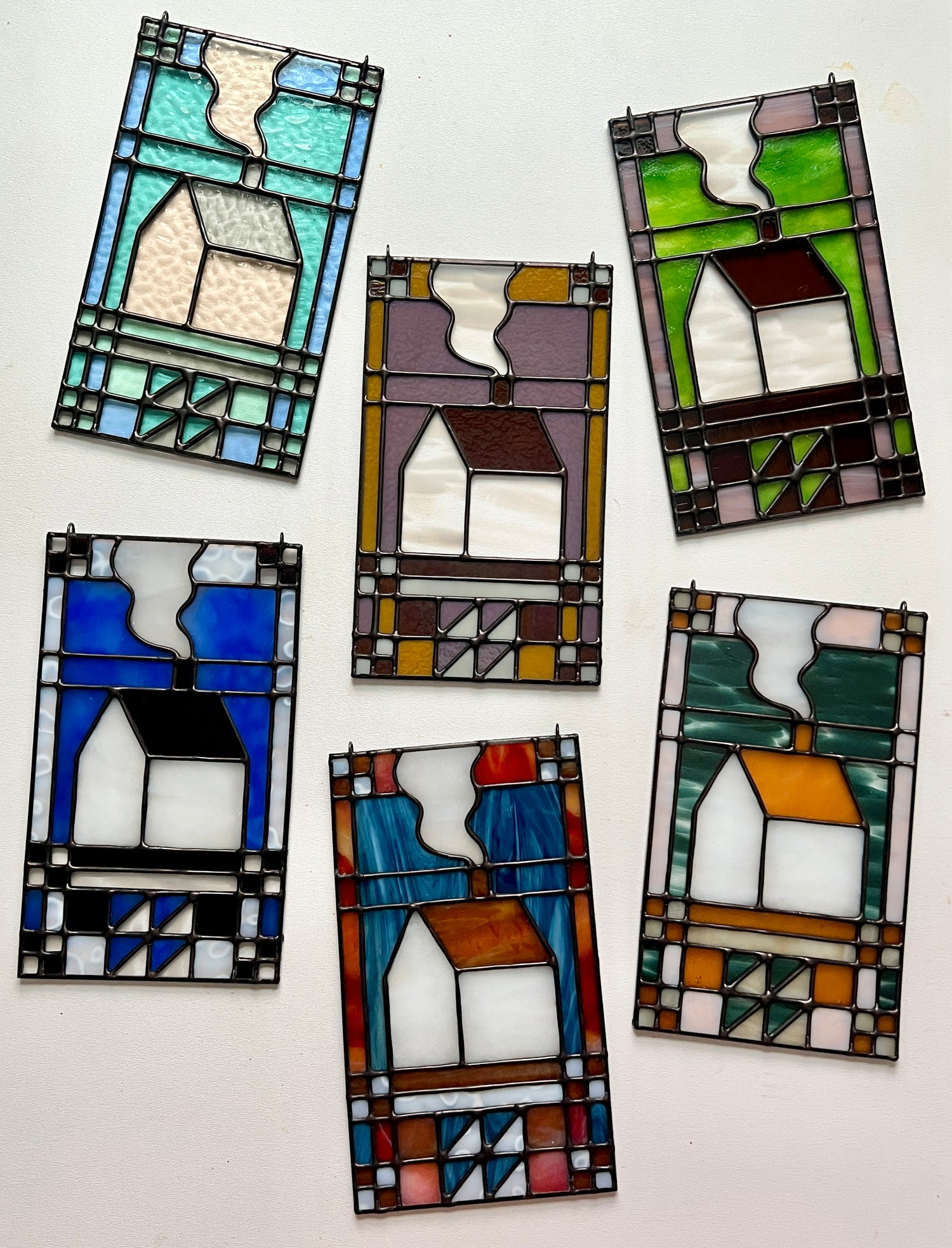 Set of six textile inspired stained glass house panels arranged in a flat lay, all art pieces in unique colorways, laying atop a white background