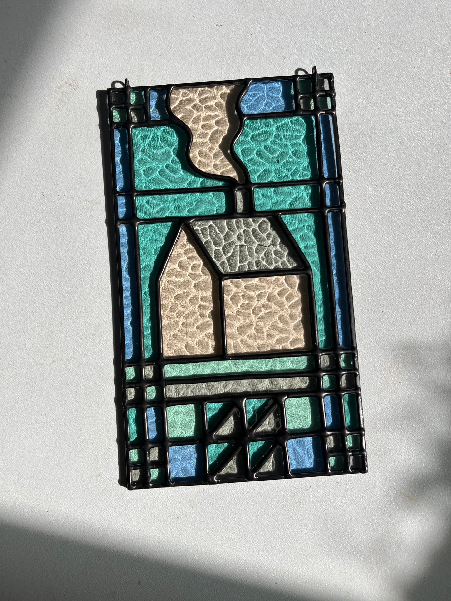 textile inspired cozy home stained glass piece in the sunlight, laying atop a white background with bright sunlight showcasing the glass texture