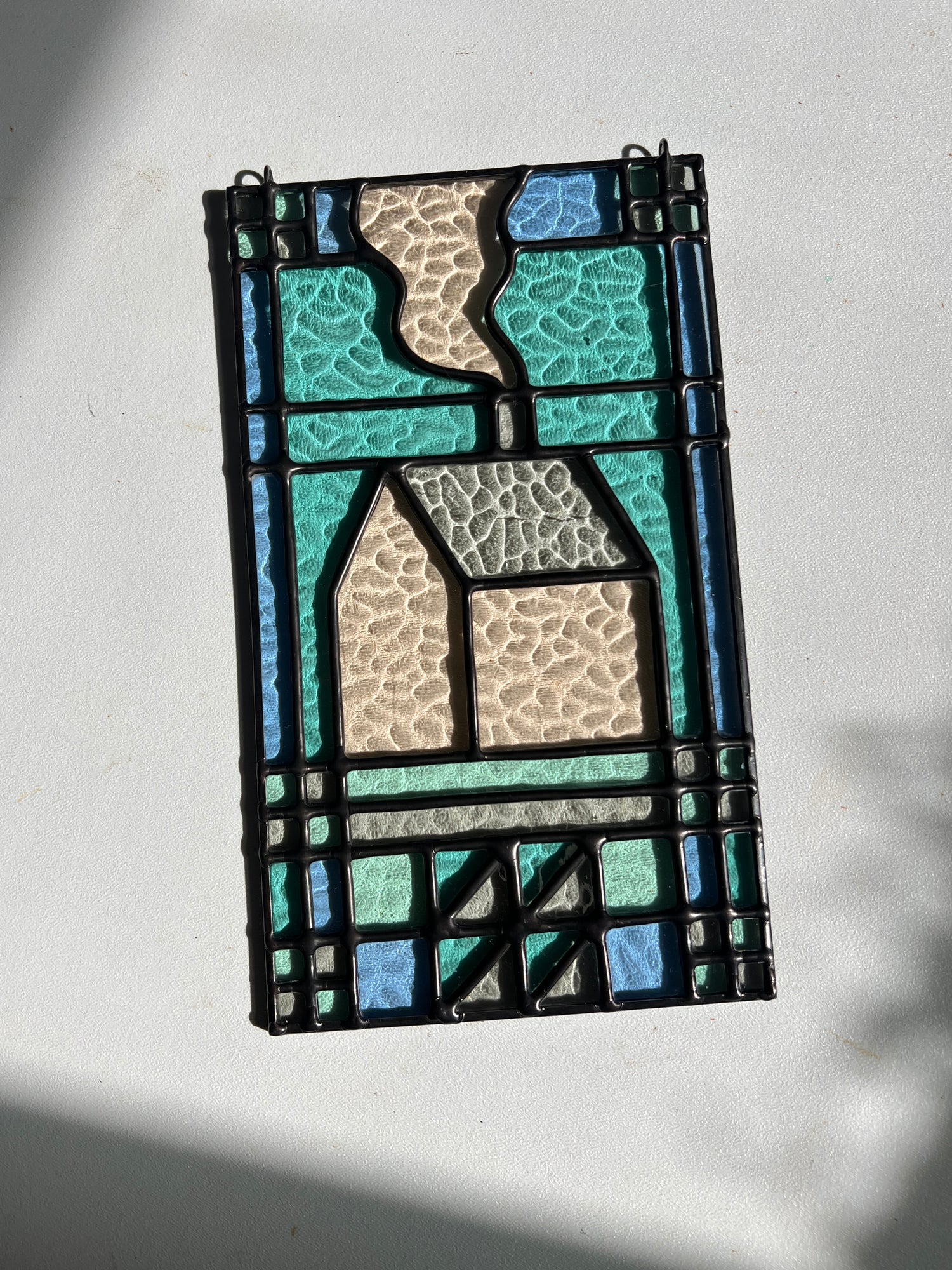 textile inspired cozy home stained glass piece in the sunlight, laying atop a white background with bright sunlight showcasing the glass texture