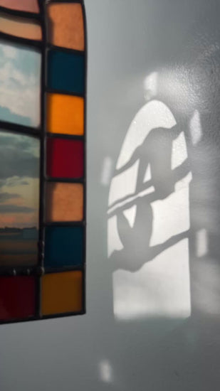Video of a stained glass panel depicting a colorful arch border, collaged photographs of sky, and two whooping cranes flying interacting with sunlight